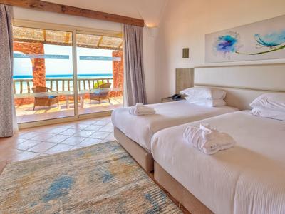 Habitación de hotel luminosa con dos camas individuales y vista a la terraza con vista al mar.