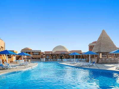 Grande piscina con acqua blu e lettini sotto un cielo azzurro in un resort.