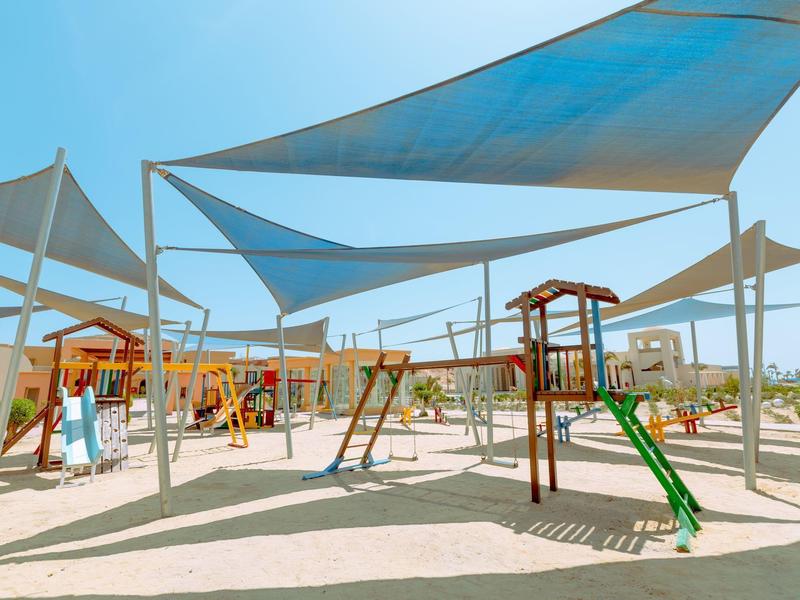 Zona de juegos para niños con estructuras de escalar y toboganes bajo toldos en un resort.