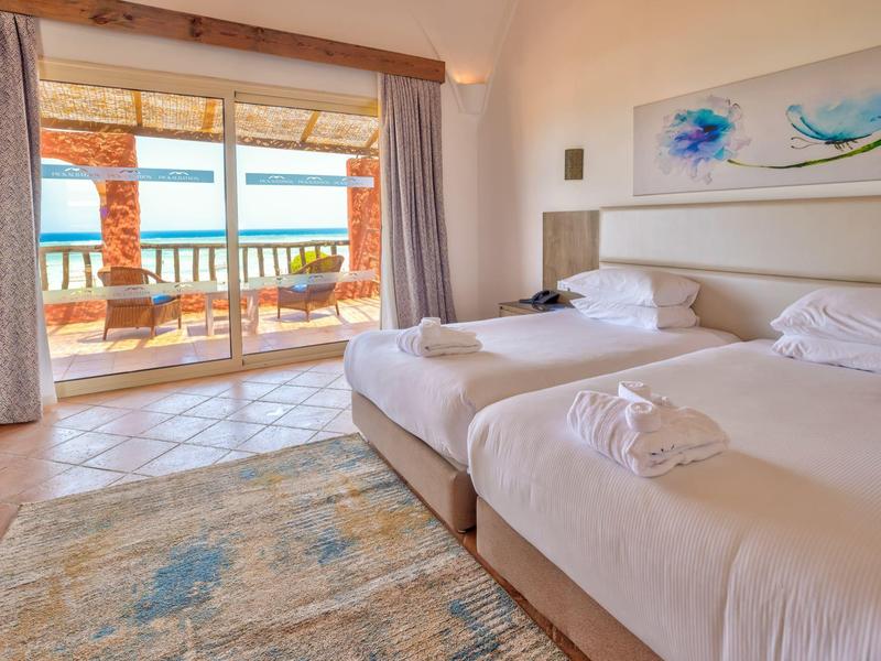 Habitación de hotel luminosa con dos camas individuales y vista a la terraza con vista al mar.