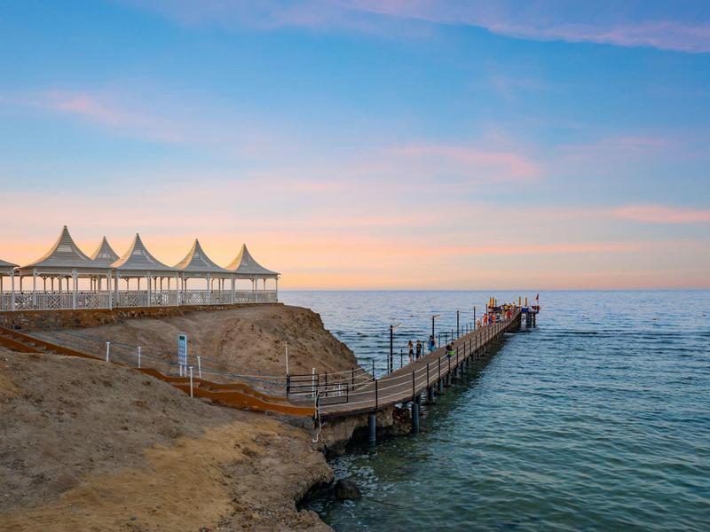 Muelle con áreas de descanso cubiertas de blanco en un acantilado sobre el mar tranquilo al atardecer.