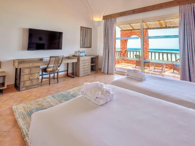 Chambre d'hôtel lumineuse avec lits doubles, bureau, TV et balcon avec vue sur la mer.