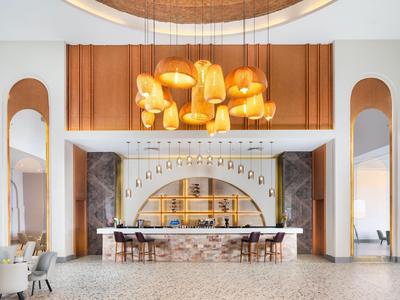 Área de bar moderna en hotel con acentos cálidos de madera y dorados y elegantes luminarias.