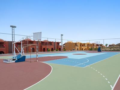 Una cancha de baloncesto con secciones de varios colores y edificios cercanos bajo un cielo despejado.