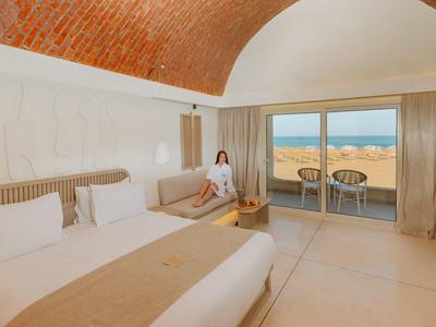 Pokój hotelowy z dużym łóżkiem, kanapą, sklepionym sufitem i balkonem z widokiem na morze.