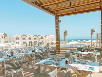 Terrazza con tavoli apparecchiati, sedie bianche e vista sul mare e hotel.