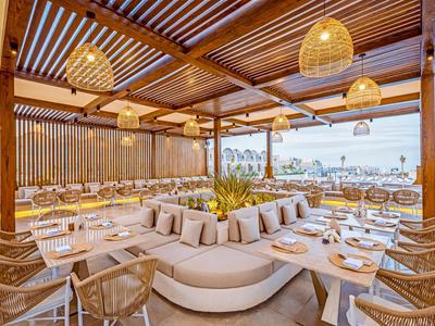 Modernes, luftiges Restaurant mit Holzbalken und Korblampen, Blick aufs Meer und bequemen Sitzgelegenheiten.