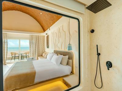 Camera d'hotel moderna con letto grande, balcone vista mare e doccia aperta.