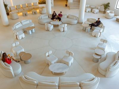 Großer heller Raum mit weißen runden Sofas und Sesseln, Menschen sitzen locker verteilt.