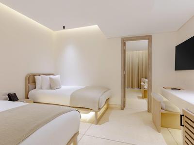 Camera d'hotel moderna con due letti singoli, pareti bianche e TV a muro.