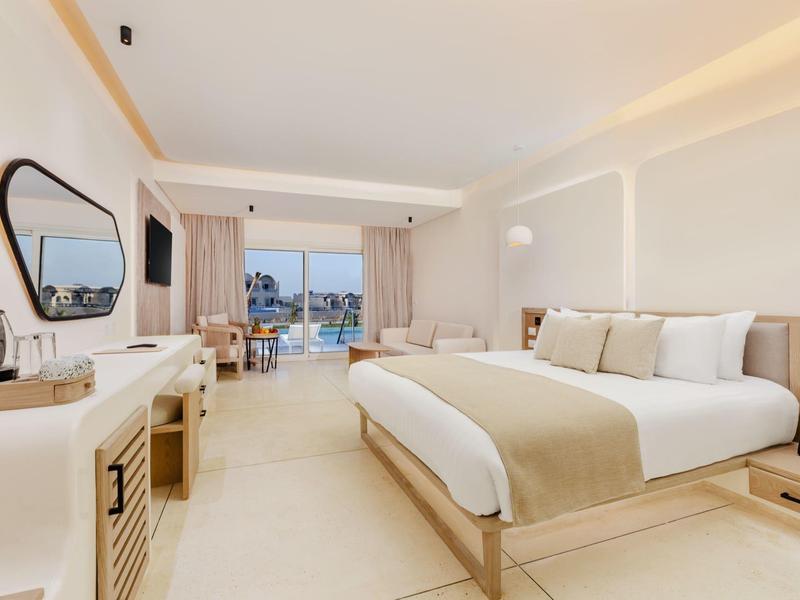 Camera d'hotel luminosa con letto grande, scrivania e balcone con vista mare.