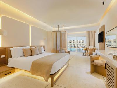 Chambre d'hôtel lumineuse avec grand lit, coin salon et balcon vue sur la mer.