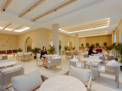 Ruime hotel lounge met beige stoelen, marmeren tafels en warme verlichting.