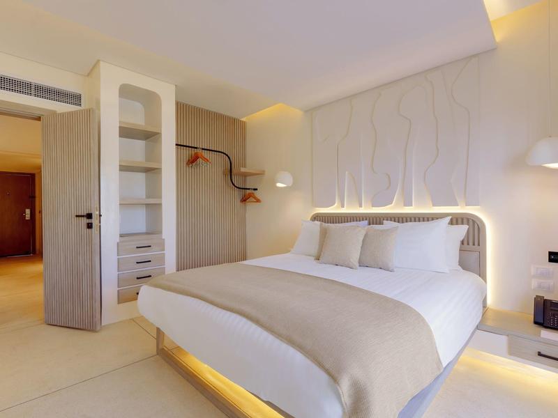 Moderne hotelkamer met een groot bed, beige accenten en zachte verlichting.