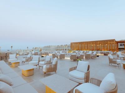 Grande terrasse sur le toit avec des fauteuils blancs et des tables en bois sous un ciel clair.