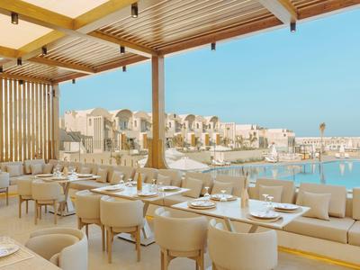 Espace de restaurant extérieur avec vue sur une piscine et des bâtiments modernes sous un ciel clair.