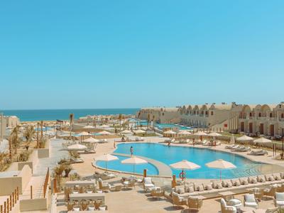 Grande piscine d'hôtel avec transats et vue sur la mer sous un ciel bleu.