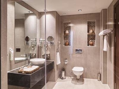 Bagno moderno con grande specchio, lavabo, WC e scalda asciugamani in toni neutri.