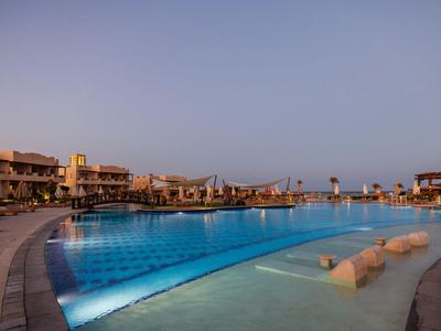 Grande piscine éclairée devant des bâtiments modernes au crépuscule.
