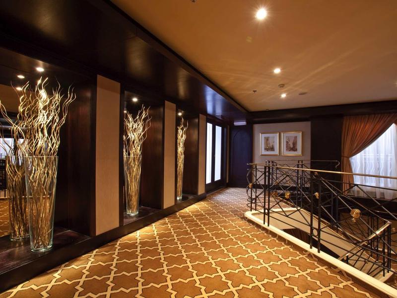 Couloir d'hôtel élégant avec grand vase, moquette à motifs et lumière tamisée.