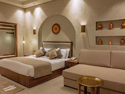 Cozy hotel room with double bed, sofa, wooden accents, and warm lighting.