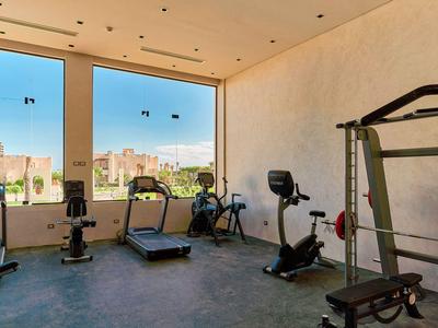 Lichte fitnessruimte met trainingsapparatuur en grote ramen met uitzicht op een stadsgezicht.