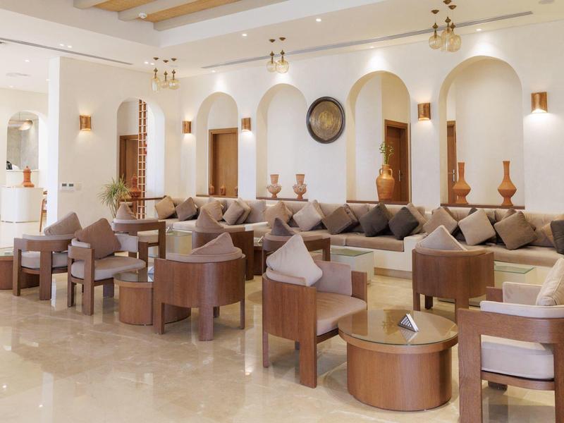 Helles, geräumiges Wohnzimmer mit hellbraunen Möbeln, Sofas, Sesseln und mehreren Kissen.