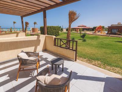 Shaded patio with chairs and table overlooking a green lawn and distant buildings.