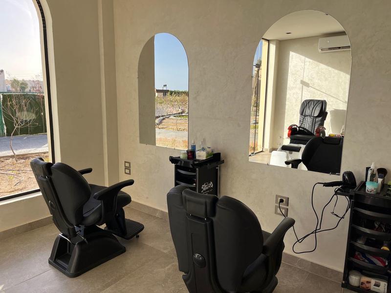 Barber chairs in a well-lit room with large arched windows and a small cabinet.