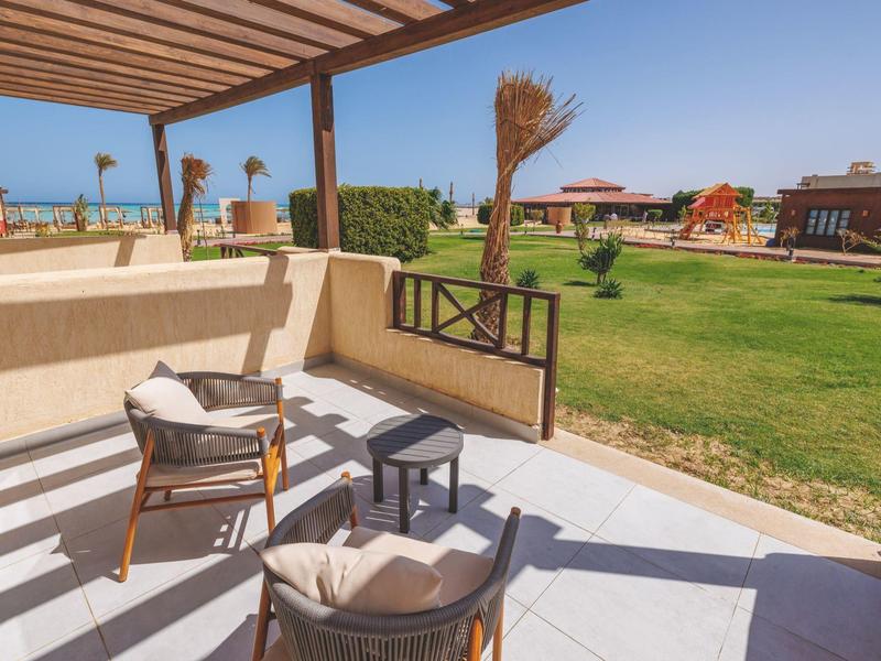 Shaded patio with chairs and table overlooking a green lawn and distant buildings.