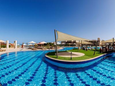 Großer Pool mit blauen Kacheln, Sonnenschirmen und Liegestühlen bei klarem Himmel.