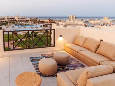 Terrazza esterna dell'hotel con divano beige, pouf, tappeto, tavolo in legno e vista mare.