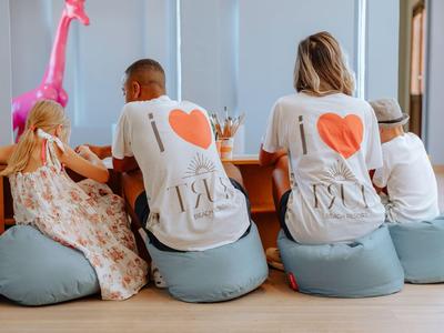 Famille en t-shirts assortis assise sur des coussins au sol à une table en bois dans un cadre chaleureux.