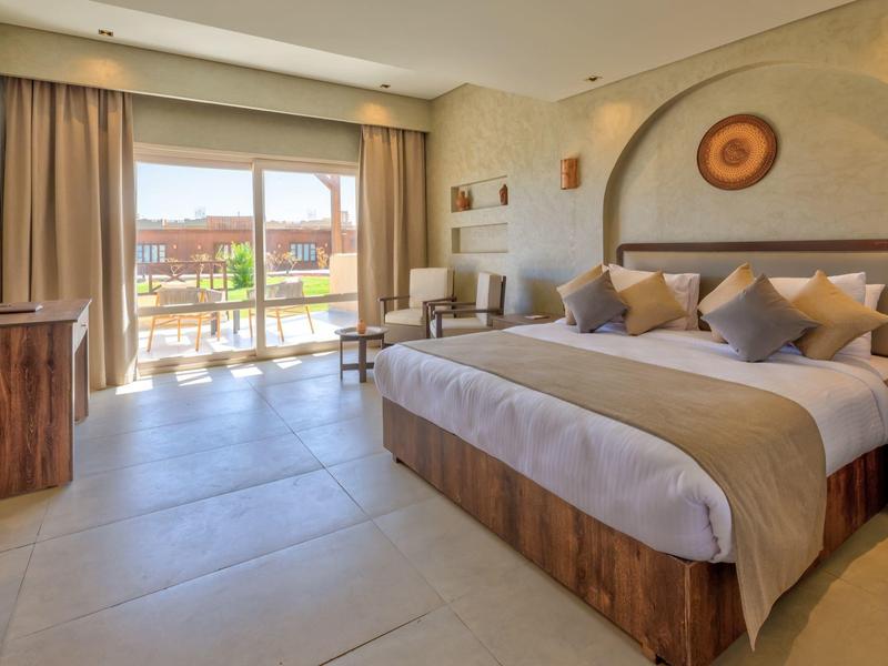 Lichte hotelkamer met tweepersoonsbed, balkon en modern houten meubilair.