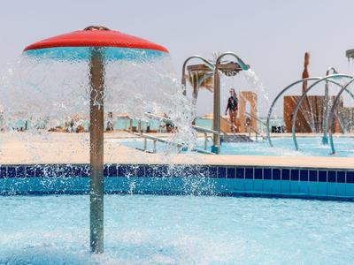 L'acqua spruzza da una fontana a fungo rossa in una piscina d'hotel con ombrelloni e lettini.