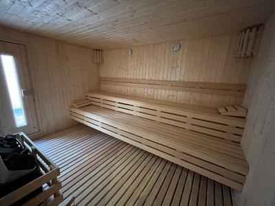 Przytulna drewniana sauna z ławkami i piecem przy drzwiach.