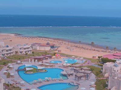 Complex avec piscines près d'une plage de sable et d'une mer bleu clair sous un ciel bleu.