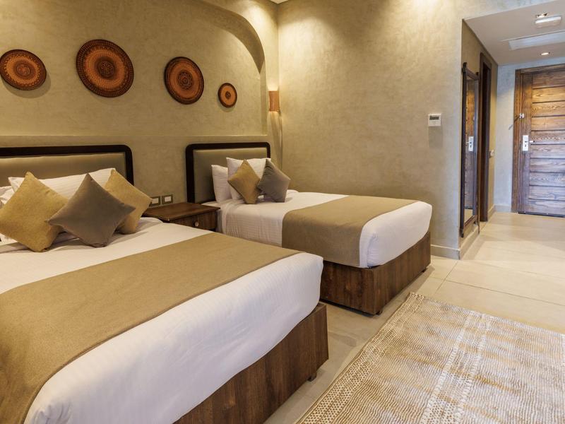 Hotelkamer met twee eenpersoonsbedden, beige decor, kussens, muurkunst en een houten deur.