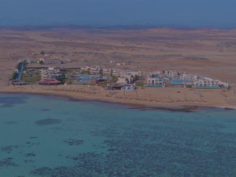Pequeña aldea costera con casas coloridas junto a una bahía marina clara y tranquila y tierra seca al fondo.