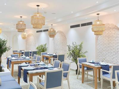 Světla restaurace s modrými židlemi, dřevěnými stoly a ratanovými stropními lampami.