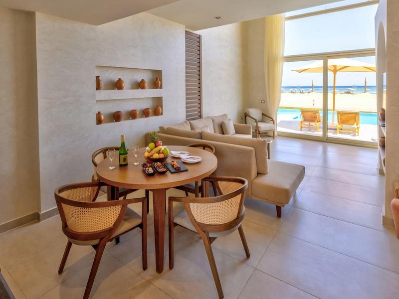 Modern dining area with round wooden table and chairs, adjoining a spacious living room with sea view.