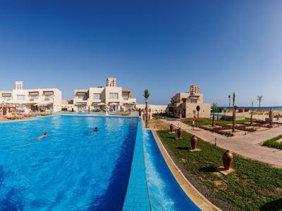 Large outdoor pool overlooking modern hotels and a well-kept garden under a sunny sky.