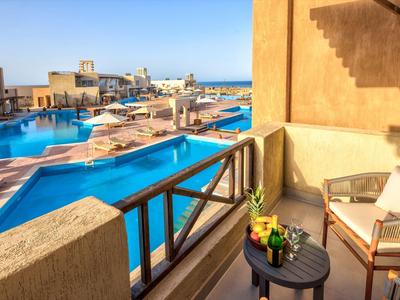 Balcony seating overlooking a large outdoor pool and distant sea under clear blue sky.