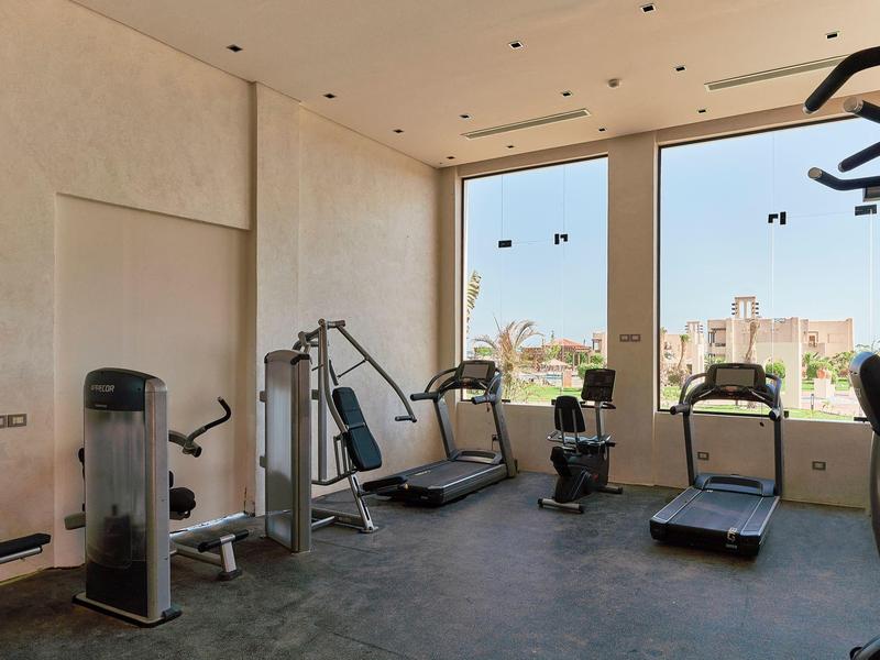 Modern fitness room with cardio and strength equipment and large windows showing city views.