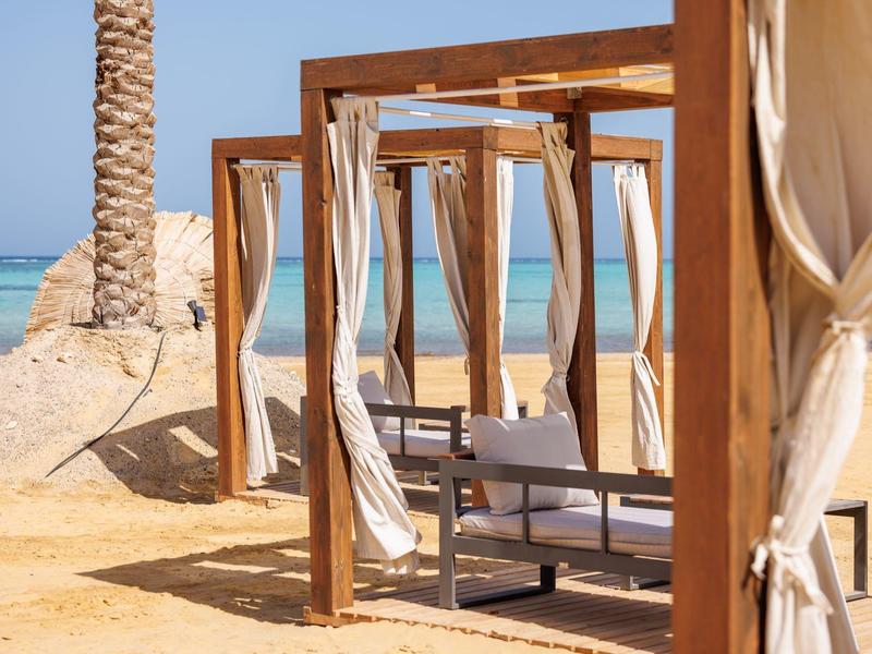 Beach with wooden cabanas, white curtains, and a view of the blue sea.