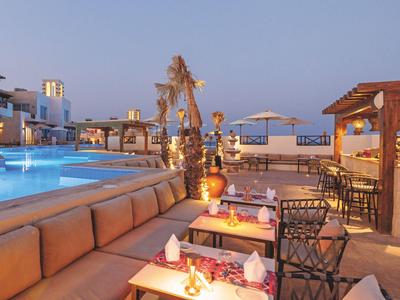 Acogedor salón junto a la piscina con asientos e iluminación al atardecer.