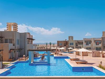 Piscine d'hôtel moderne avec mobilier lounge bleu et transats sous un ciel dégagé.