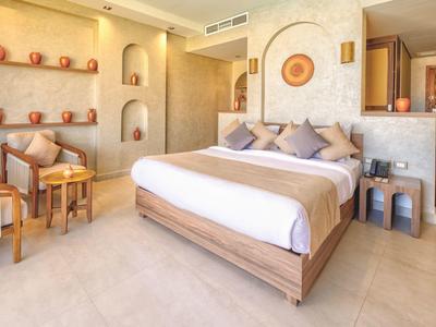 Bright hotel room with double bed, beige walls, wooden furniture, and decorative wall niches.