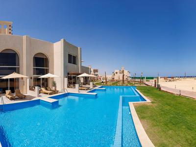 Hotel moderno con grande piscina accanto a una spiaggia sabbiosa sotto un cielo blu limpido.