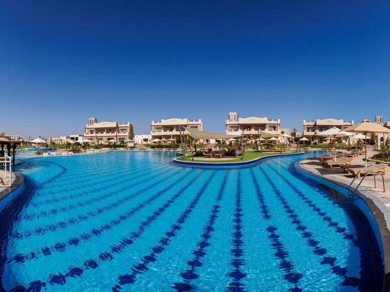 Large outdoor pool with clear blue water and sunny sky at a resort.